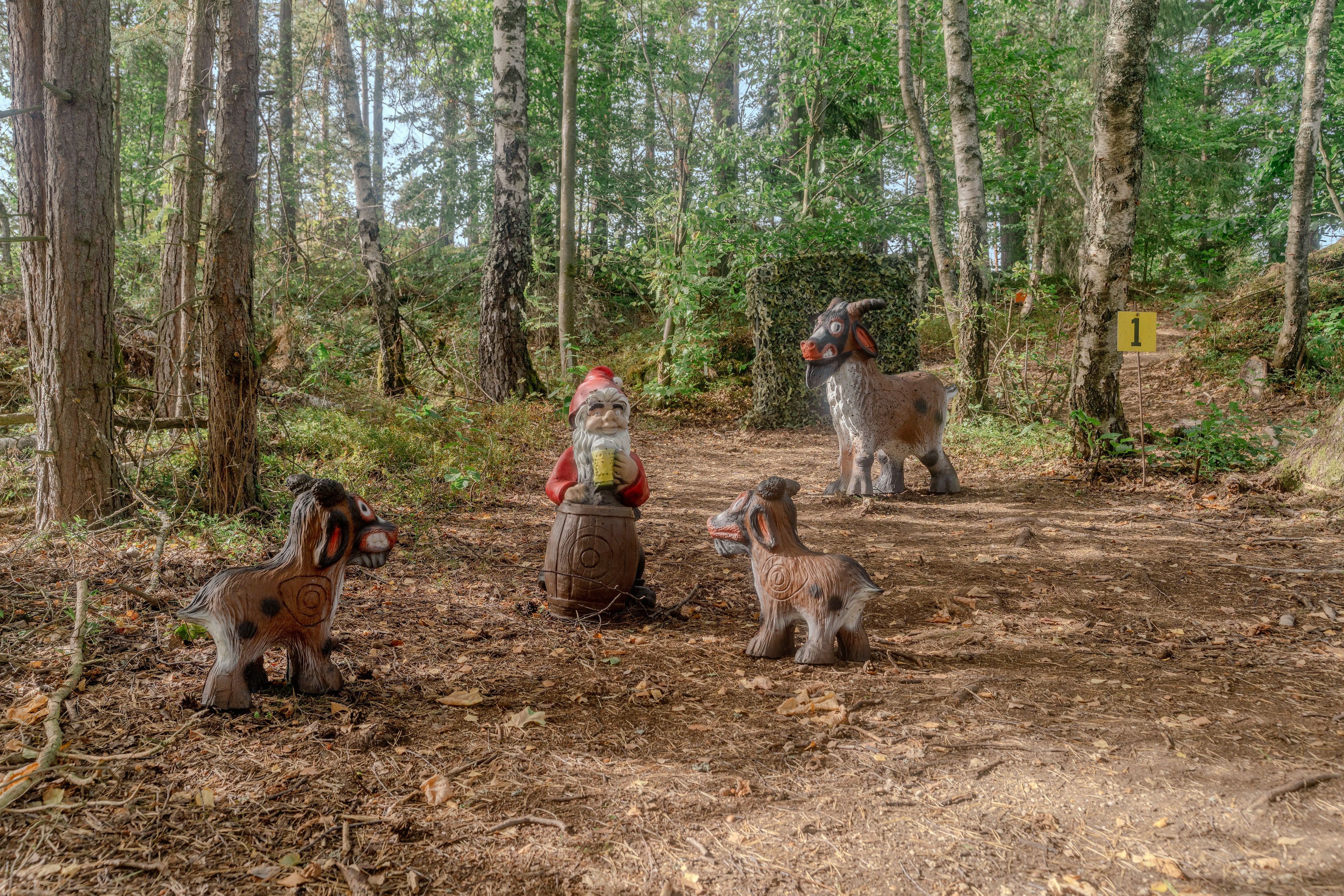 Mehrere 3D-Tierziele und ein Gartenzwerg auf einem Fass in einer Waldlandschaft des Bogenparcours im Naturpark Nordwald